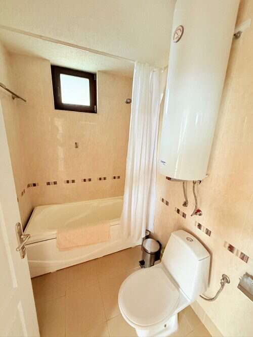 Bright bathroom featuring a bathtub, toilet, and small window for natural light.