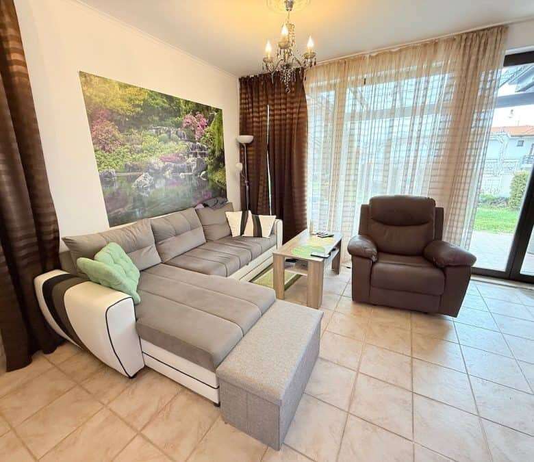 Bright living room with sofa, armchair, and scenic garden view through glass doors.