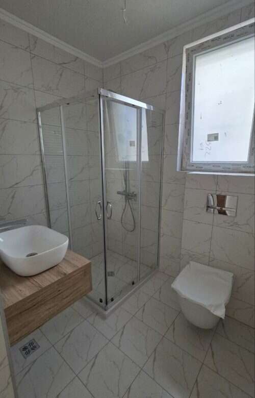 Bathroom with glass shower enclosure, white marble tiles, and contemporary fixtures.