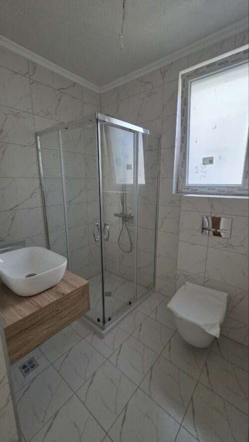 Bathroom with glass shower enclosure, white marble tiles, and contemporary fixtures.