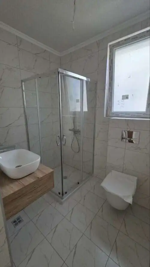 Bathroom with glass shower enclosure, white marble tiles, and contemporary fixtures.