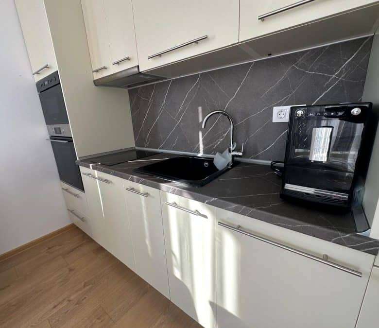 Kitchen with black countertop, sink, and appliances in a sunny apartment.