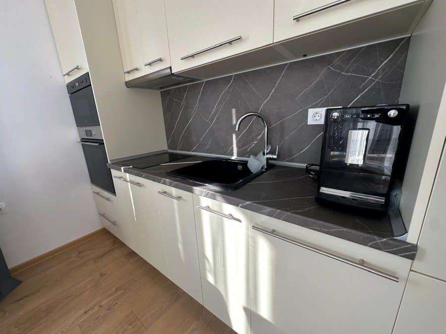 Kitchen with black countertop, sink, and appliances in a sunny apartment.