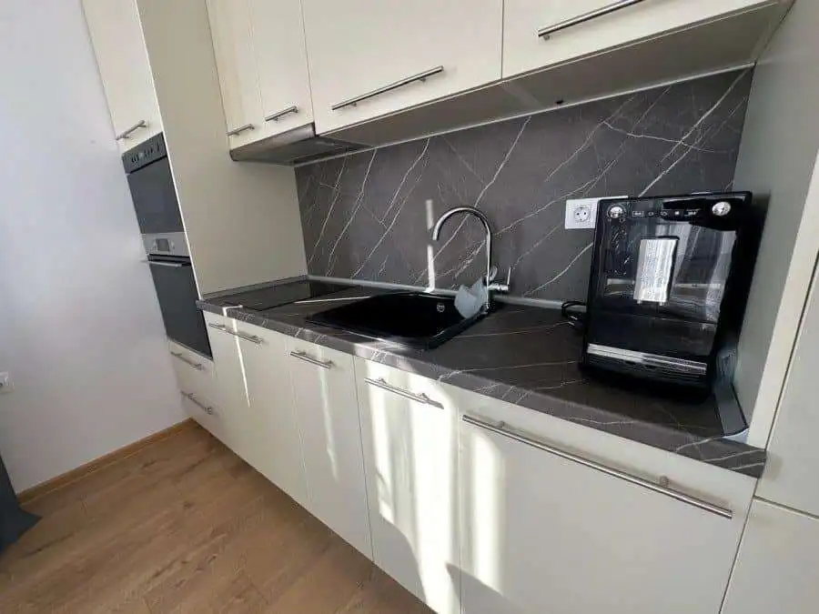 Kitchen with black countertop, sink, and appliances in a sunny apartment.