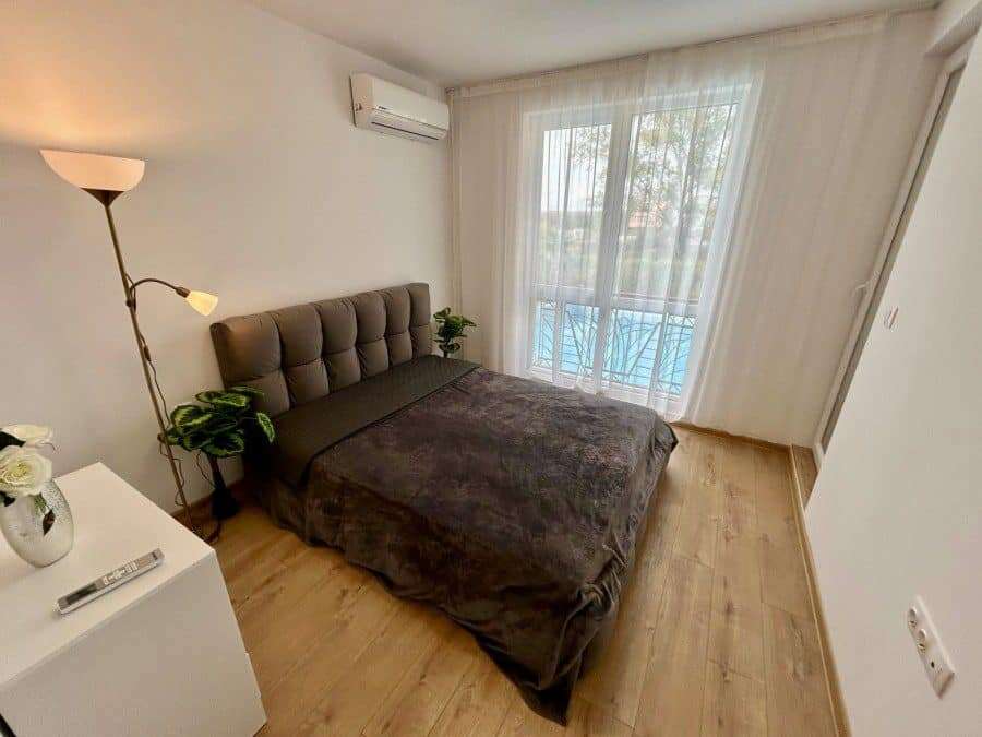 Comfortable bedroom featuring a large bed, stylish decor, and balcony overlooking the pool area. Per.