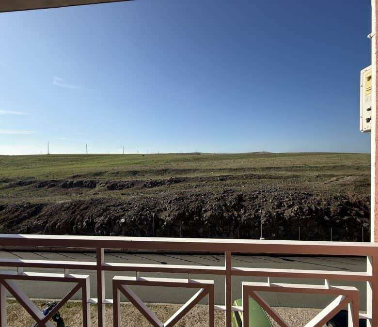 Balcony view from a fully furnished 1-bedroom, 2-bath apartment overlooking open fields on a sunny d.