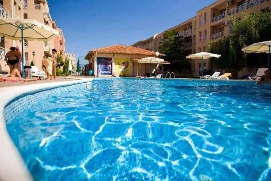 Pool with clear blue water at a sunny apartment complex with umbrellas and residents relaxing.