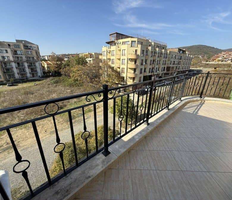 Balcony with black wrought iron railing overlooking residential buildings and green landscape in Sve.