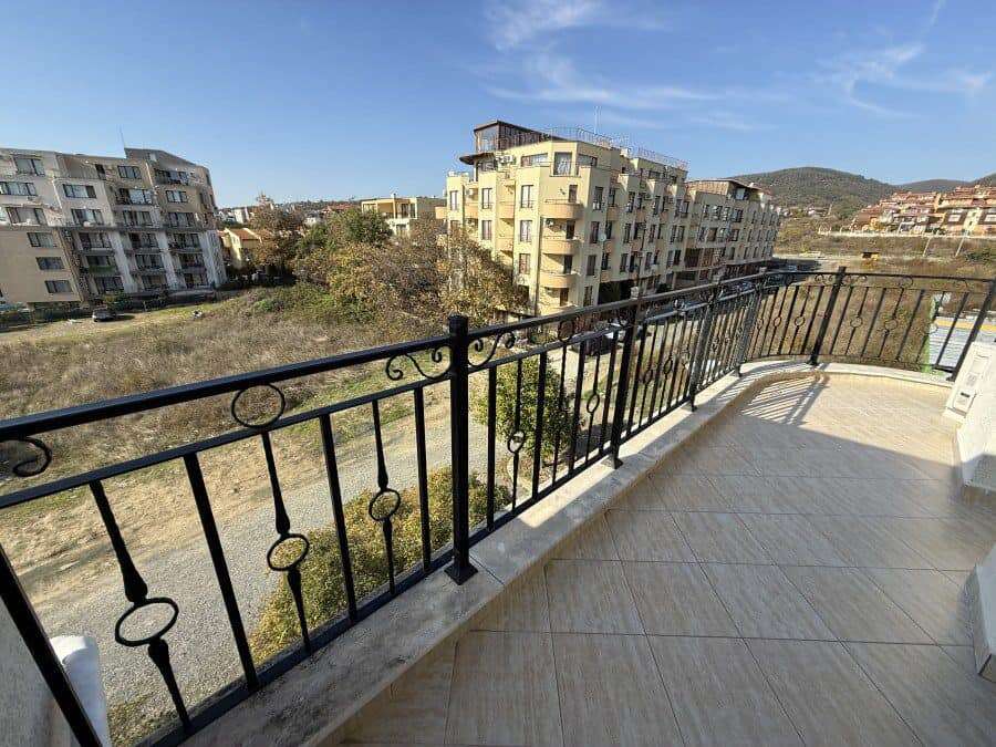 Balcony with black wrought iron railing overlooking residential buildings and green landscape in Sve.