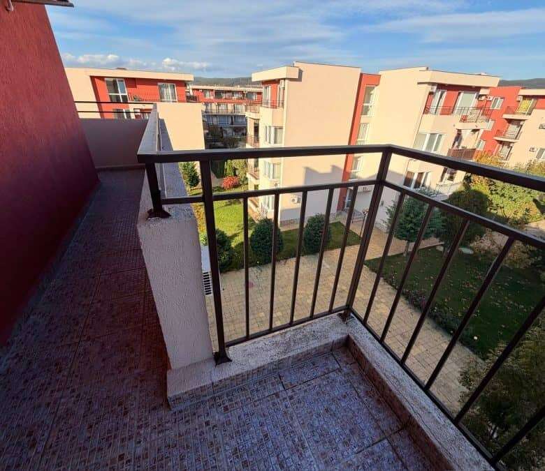 Balcony with black metal railing overlooking the complex and green outdoor areas.