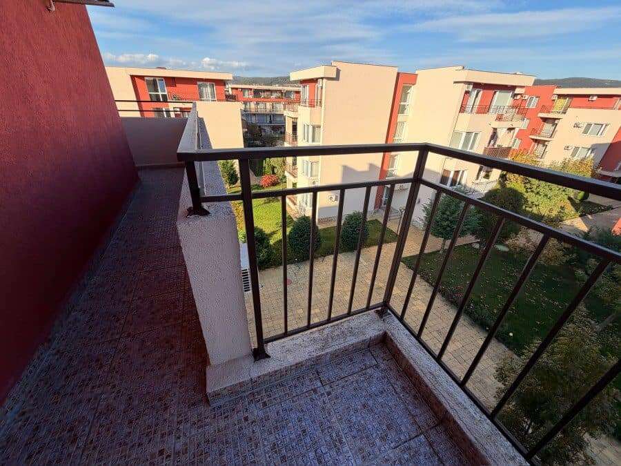 Balcony with black metal railing overlooking the complex and green outdoor areas.