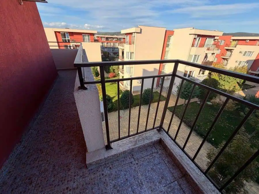 Balcony with black metal railing overlooking the complex and green outdoor areas.