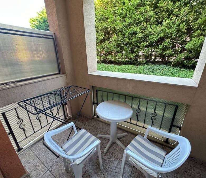 Balcony with two chairs, small table, and lush green background at Prestige Fort Beach.