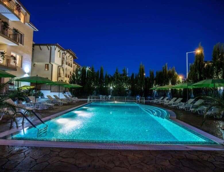 Brightly lit swimming pool surrounded by sun loungers and umbrellas.