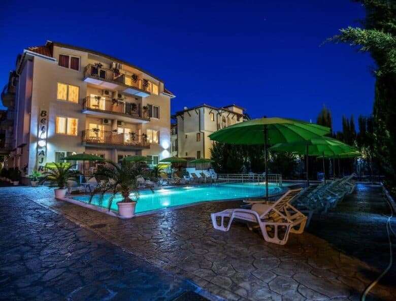Brightly lit apartment building with pool and outdoor seating at night.