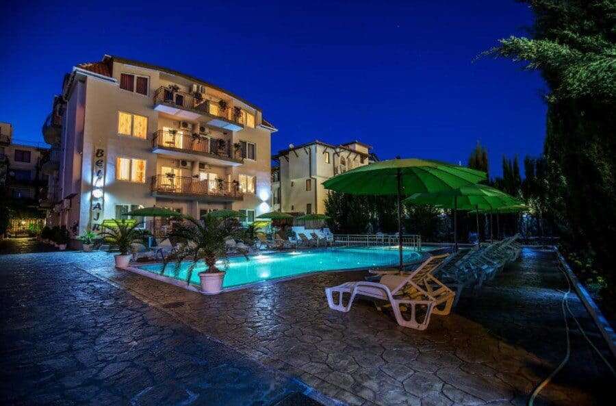 Brightly lit apartment building with pool and outdoor seating at night.