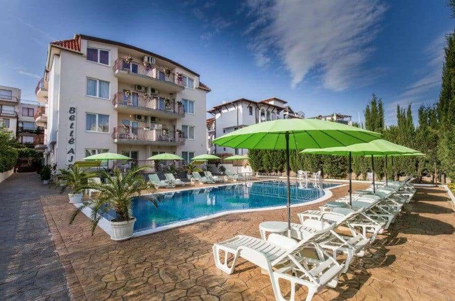 Bright outdoor pool area with sun loungers and green umbrellas near Belle Air.