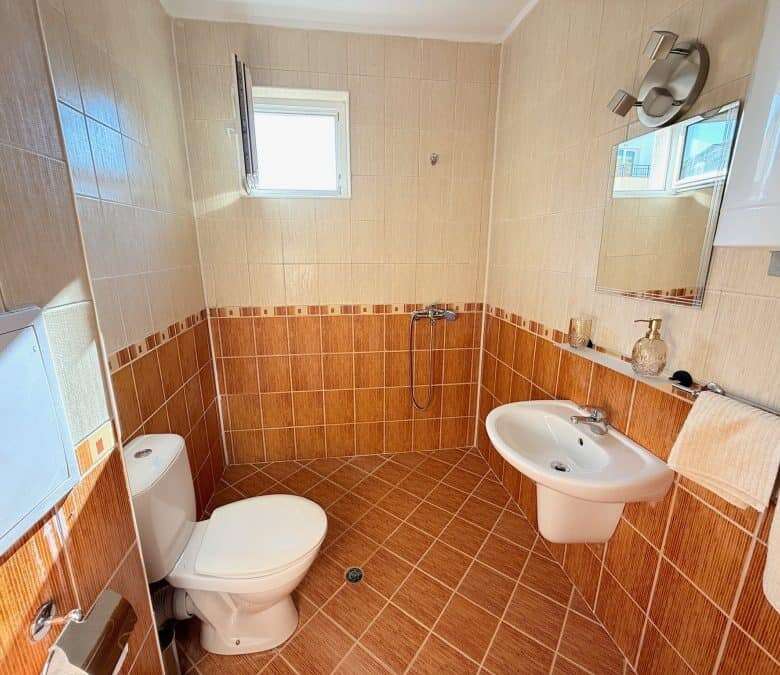 Bathroom with toilet, sink, and mirror in a bright, clean space.