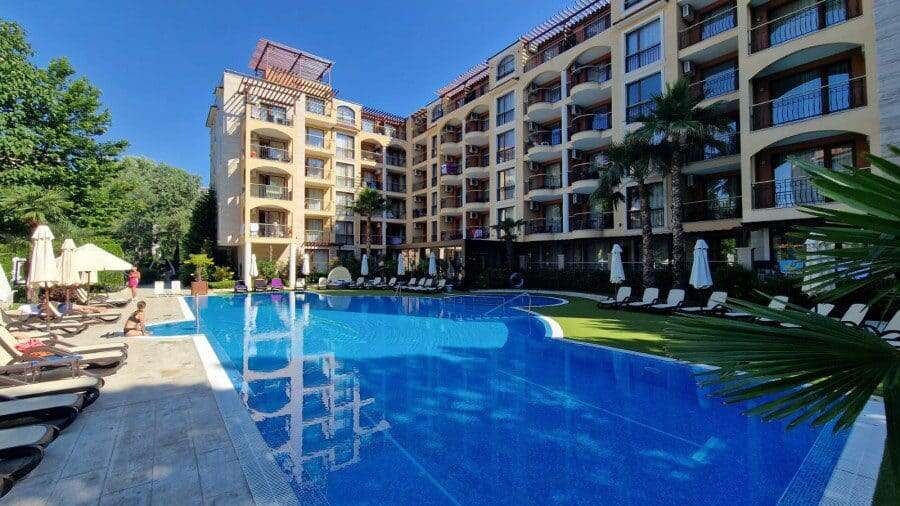 Pool view of a 1-bedroom apartment at Harmony Suites, featuring a large swimming pool and lush tropi.