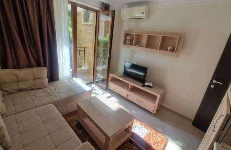 Interior of a living room with sofa, TV, and balcony access in a sunny apartment.