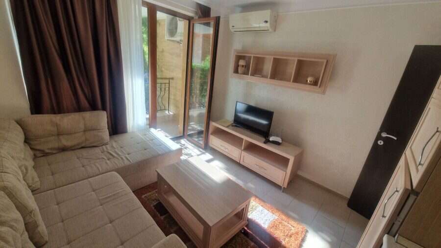 Interior of a living room with sofa, TV, and balcony access in a sunny apartment.