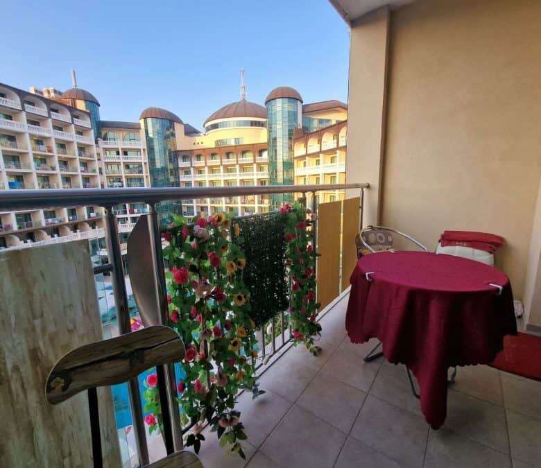 Balcony view of Sunny Beach with colorful flowers, a small table, and chairs overlooking nearby hote.