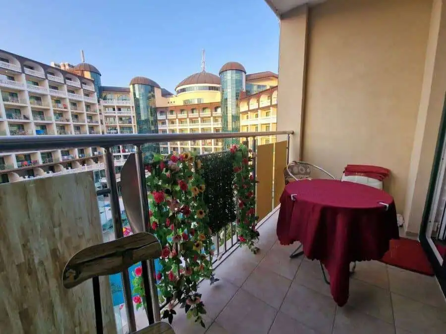Balcony view of Sunny Beach with colorful flowers, a small table, and chairs overlooking nearby hote.