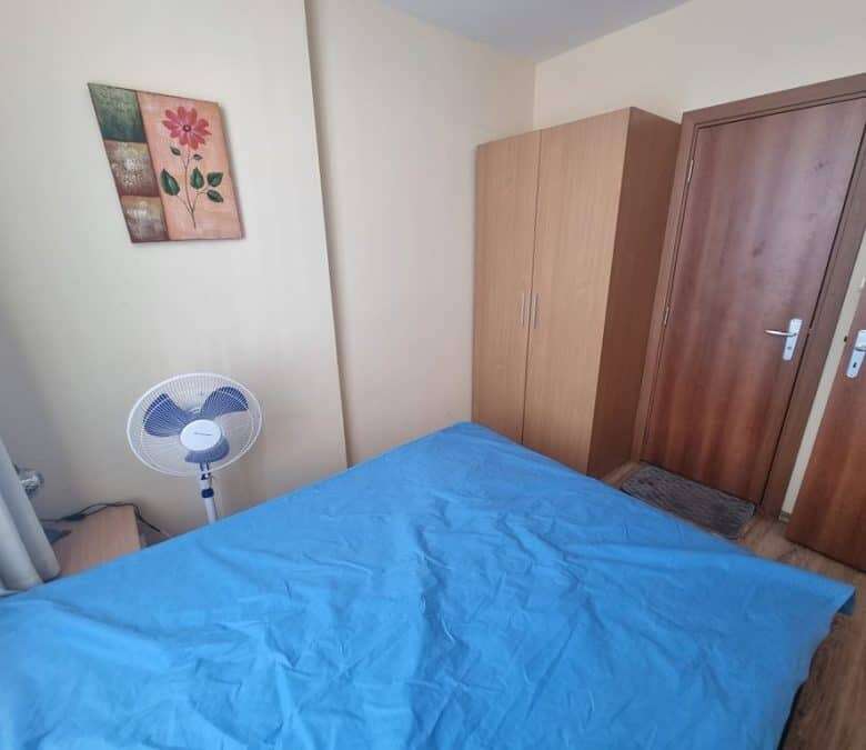 Interior view of a 1-bedroom apartment in Dawn Park, Sunny Beach with a blue bed and wooden furnitur.
