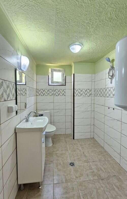 Bright renovated bathroom with white sink, toilet, and tiled walls in a spacious home.