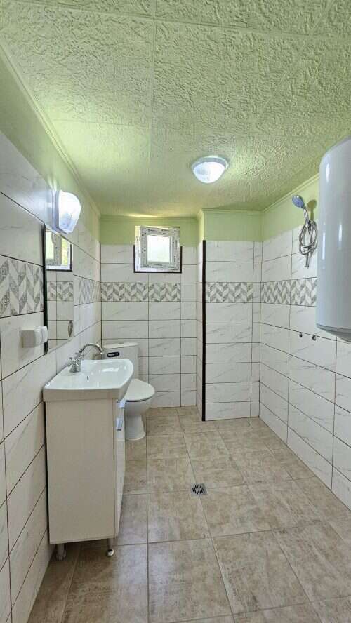 Bright renovated bathroom with white sink, toilet, and tiled walls in a spacious home.