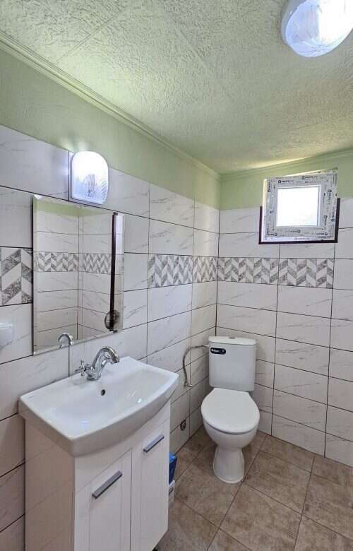 Bright bathroom with new sink, mirror, and toilet in a renovated house.