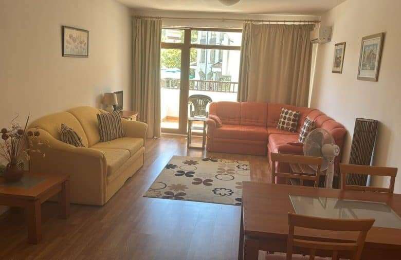 Bright living room with sofas and balcony overlooking greenery, near the sea.