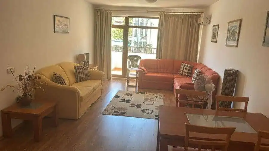 Bright living room with sofas and balcony overlooking greenery, near the sea.