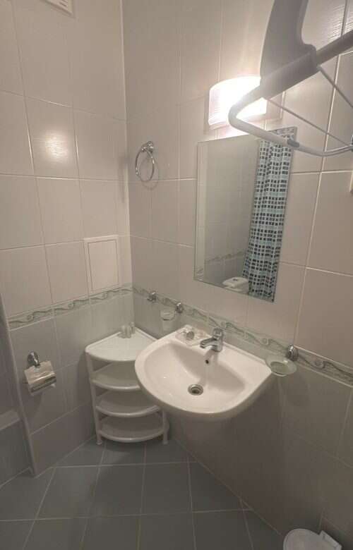 Small bathroom with sink, mirror, and tiled walls in a furnished apartment.