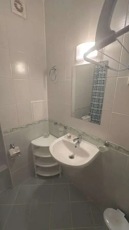 Small bathroom with sink, mirror, and tiled walls in a furnished apartment.