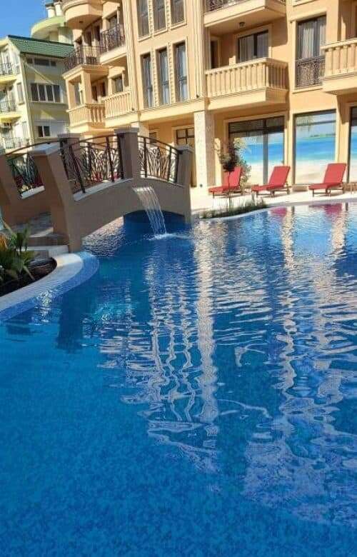 Pool area of a modern apartment building at Sunny Beach with sun loungers and a small bridge.