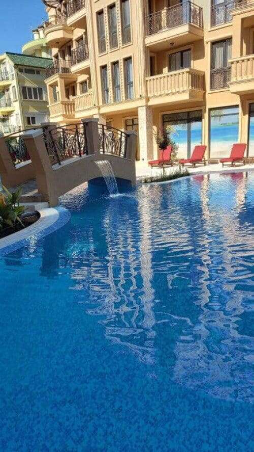 Pool area of a modern apartment building at Sunny Beach with sun loungers and a small bridge.