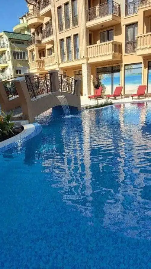 Pool area of a modern apartment building at Sunny Beach with sun loungers and a small bridge.