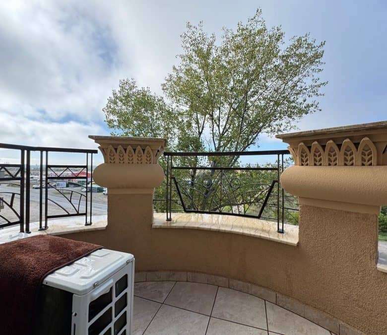 Balcony with ornate columns and black railing overlooking lush greenery and sky in Sunny Beach, Bulg.
