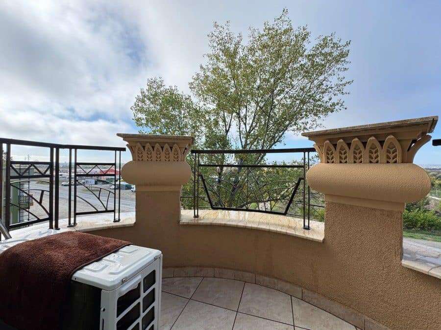 Balcony with ornate columns and black railing overlooking lush greenery and sky in Sunny Beach, Bulg.