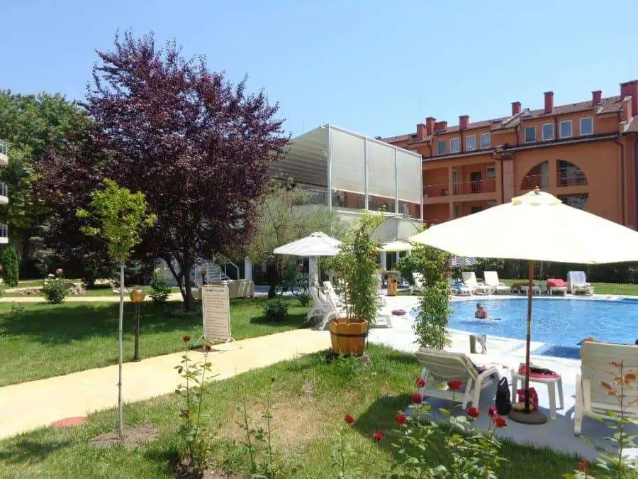 Poolside garden with lounge chairs, umbrellas, and lush greenery at Oasis, Ravda.