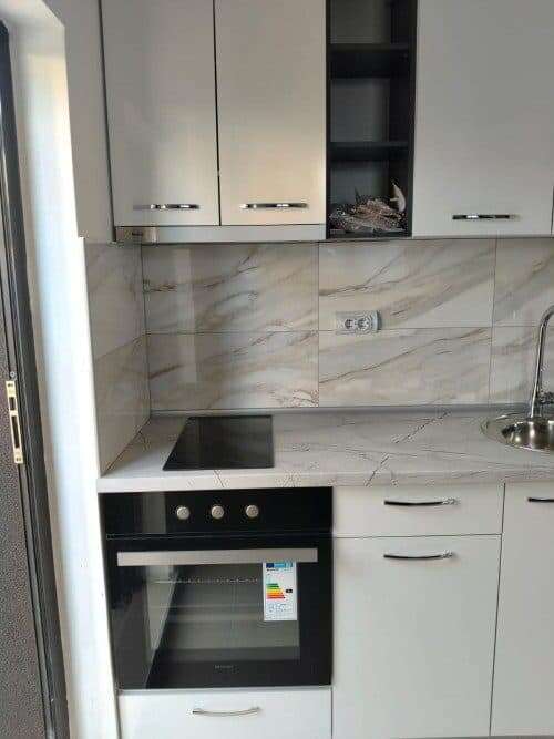 Modern kitchen with white cabinets, marble backsplash, and built-in oven in Sunny Beach, Bulgaria.
