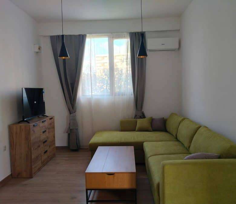 Bright living room with green sofa, TV, and large window with curtains.