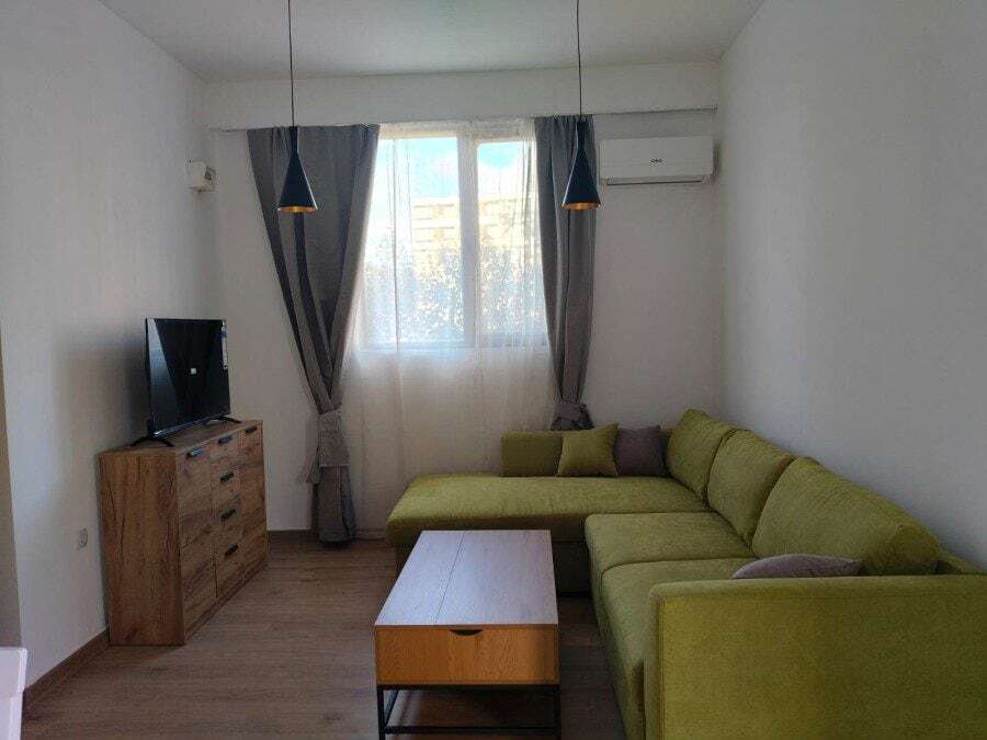 Bright living room with green sofa, TV, and large window with curtains.