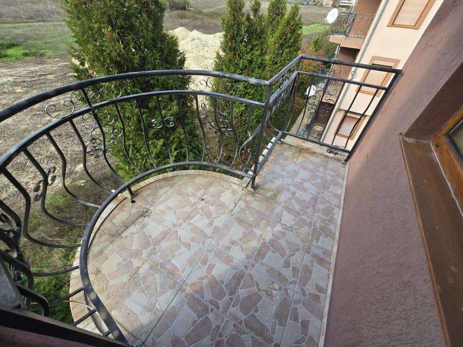 Cozy balcony with wrought iron railing overlooking greenery Balcony of a fully furnished 1-bedroom apartment near Ravda beach, featuring decorative tile floorin.