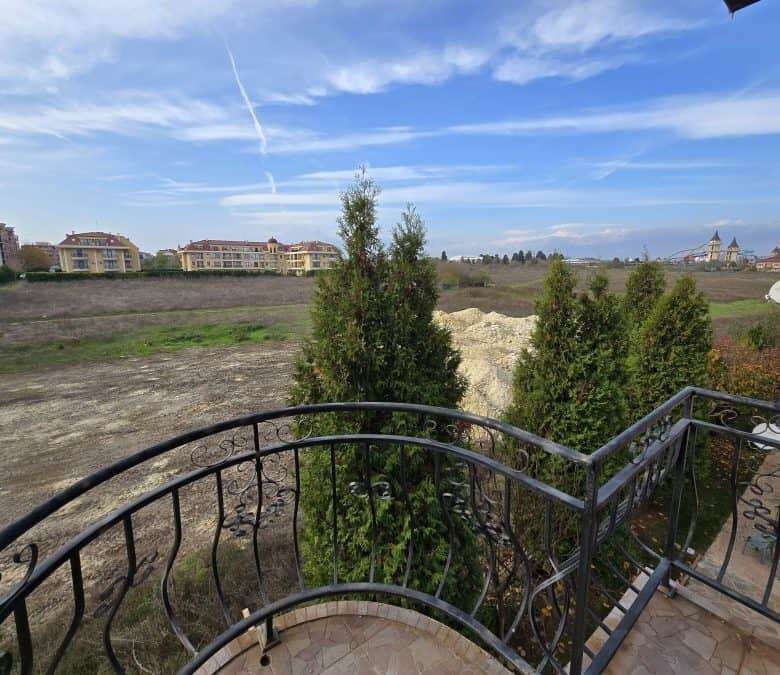 Balcony view of Ravda with trees, buildings, and blue sky.