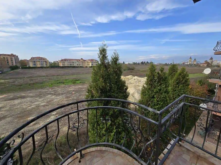 Balcony view of Ravda with trees, buildings, and blue sky.