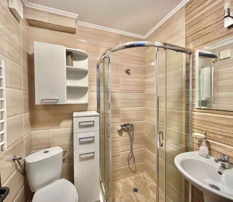 Bright bathroom with shower enclosure, toilet, and sink in a seaside apartment.