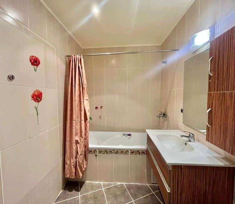 Bright bathroom featuring bathtub, sink, and wooden storage unit.