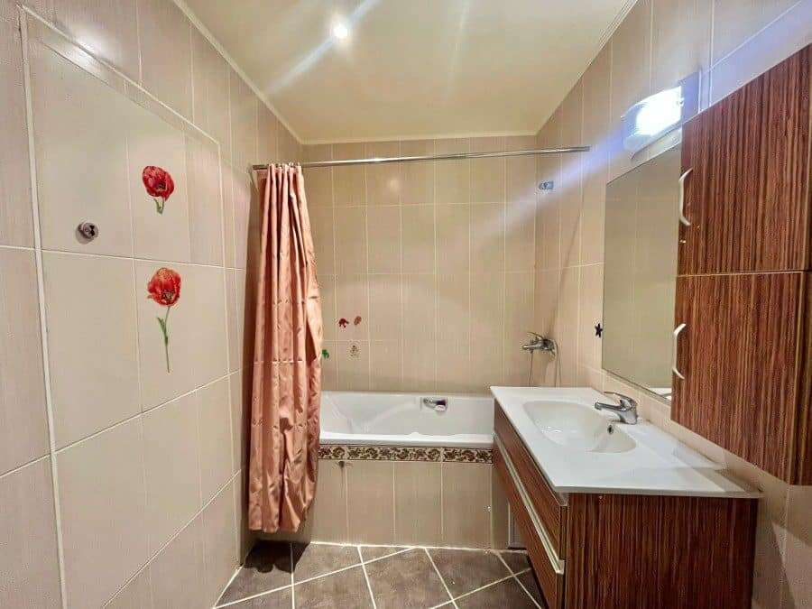 Bright bathroom featuring bathtub, sink, and wooden storage unit.